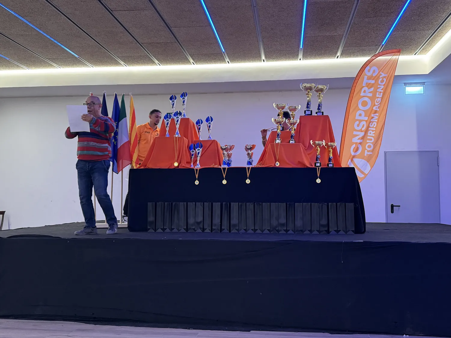 Presentador en el escenario junto a la mesa de trofeos del torneo de Santa Susanna
