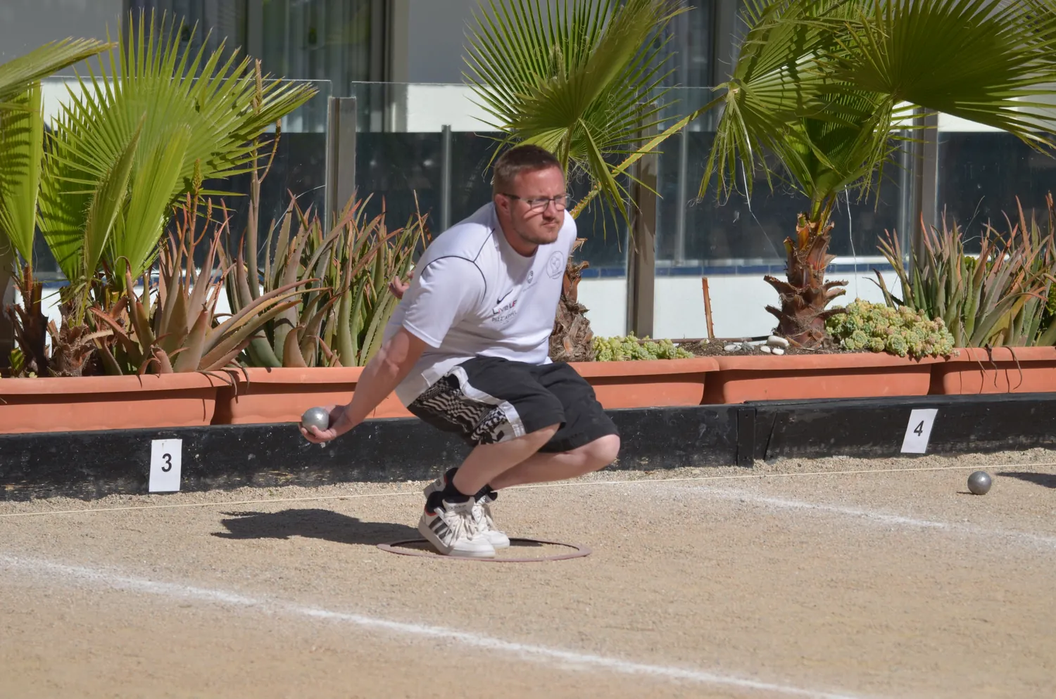Giocatore accovacciato prepara il lancio al torneo di petanque di Santa Susanna